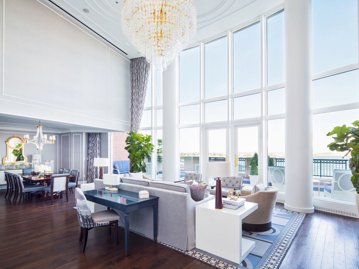 Elegant room with large windows, chandelier, sofas, and dining area.