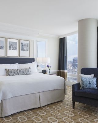 A well-appointed hotel room with a large bed, accent chair, and city view.