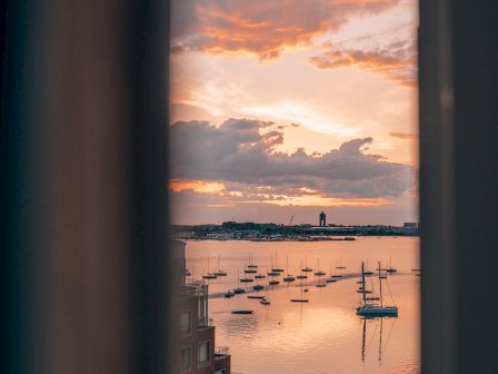 A serene view through a window showing a sunset, boats on water, and buildings.