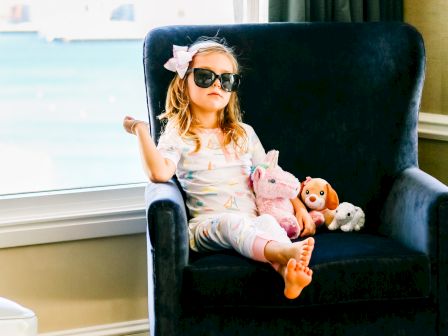 A child sits in a chair with sunglasses and a toy, exuding confidence.