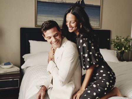 A smiling couple in a cozy embrace, seated on a bed in a room.