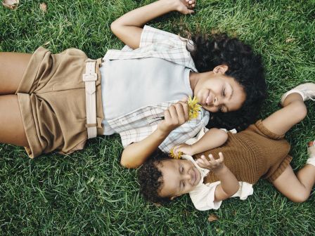 Two children are lying on grass, smiling, sharing a pleasant moment together.