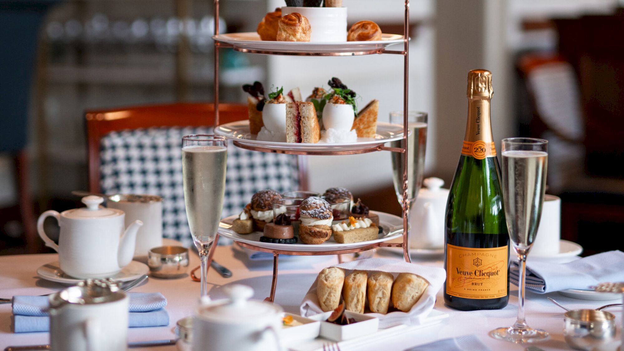 An elegant afternoon tea setup with pastries, champagne, and a teapot.