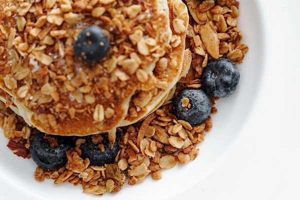 A stack of pancakes with granola and blueberries on top.