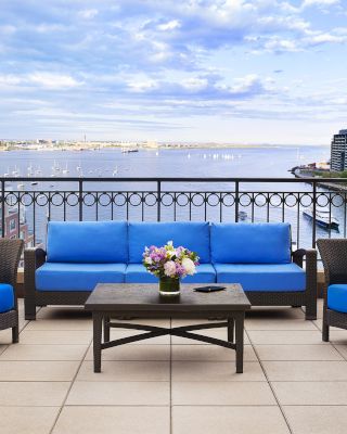 A balcony with blue sofas, table, and flowers overlooking a waterfront view.