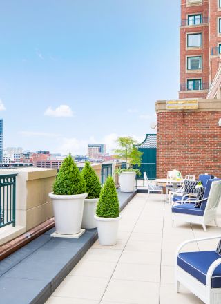 A balcony with chairs, tables, and potted plants overlooking a cityscape.