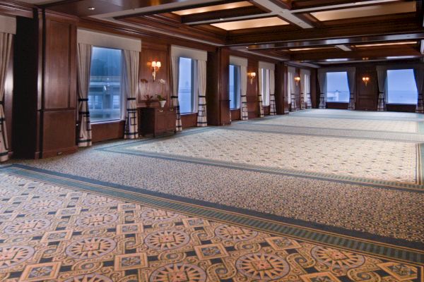 An empty banquet hall with patterned carpet, wood panels, and long drapes