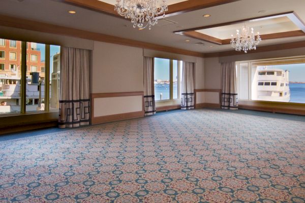 An empty room with patterned carpet, chandeliers, and a view of