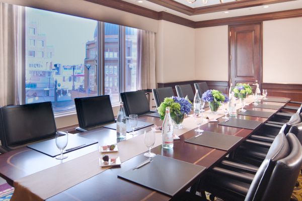 A boardroom with a long table, chairs, laptops, and a city view