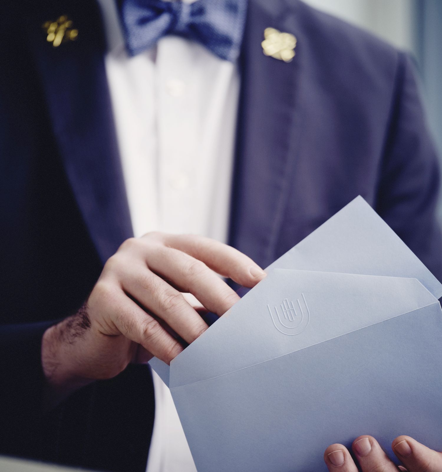 A person in a suit with a bow tie is holding an envelope.