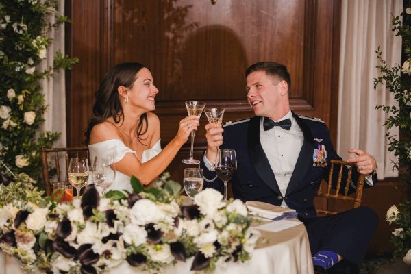 A couple is toasting with champagne, surrounded by elegant floral arrangements.