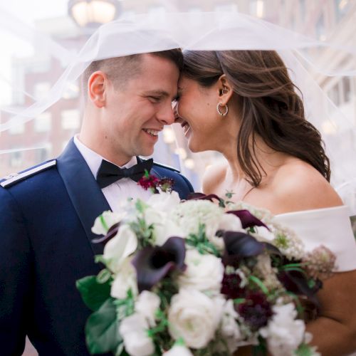 A bride and groom smiling at each other, with a bouquet and veil.