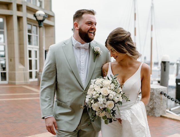 A couple in wedding attire is walking hand in hand, smiling joyfully.