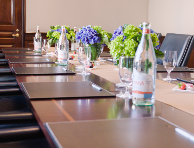 A modern boardroom with a long table, chairs, water bottles, glasses,