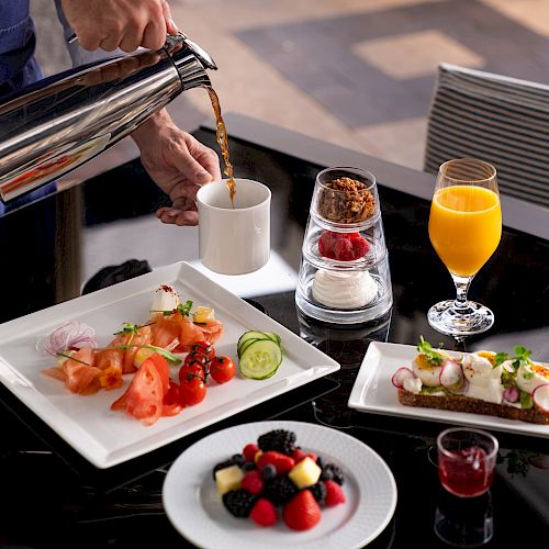 Elegant breakfast setup with various dishes and a person pouring a drink.