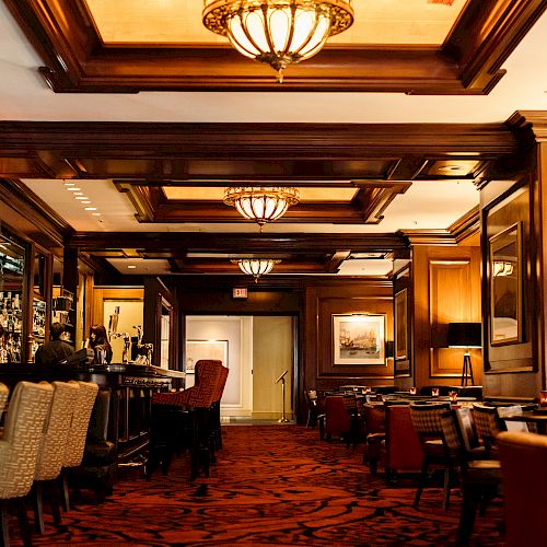 Elegant interior with wooden bar, chairs, tables, and ornate ceiling lights.