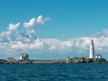 A lighthouse stands on a rocky shore with clouds above the blue sea.