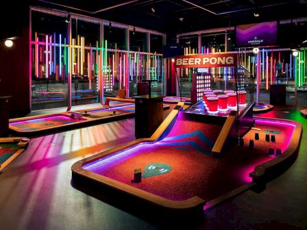 A neon-lit room with mini-golf and beer pong areas.