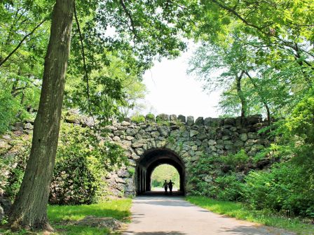 A stone arch bridge over a pathway surrounded by lush greenery and two people in
