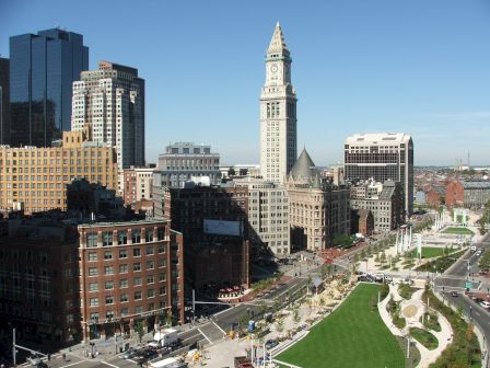 Cityscape with historic clock tower, buildings, green park space, and clear blue