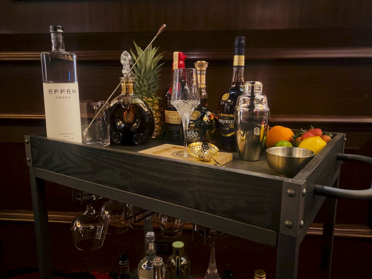 A bar cart with various bottles, fruits, and a cocktail shaker.
