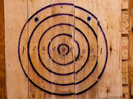 Wooden archery or dartboard target with scored marks, mounted on a wall
