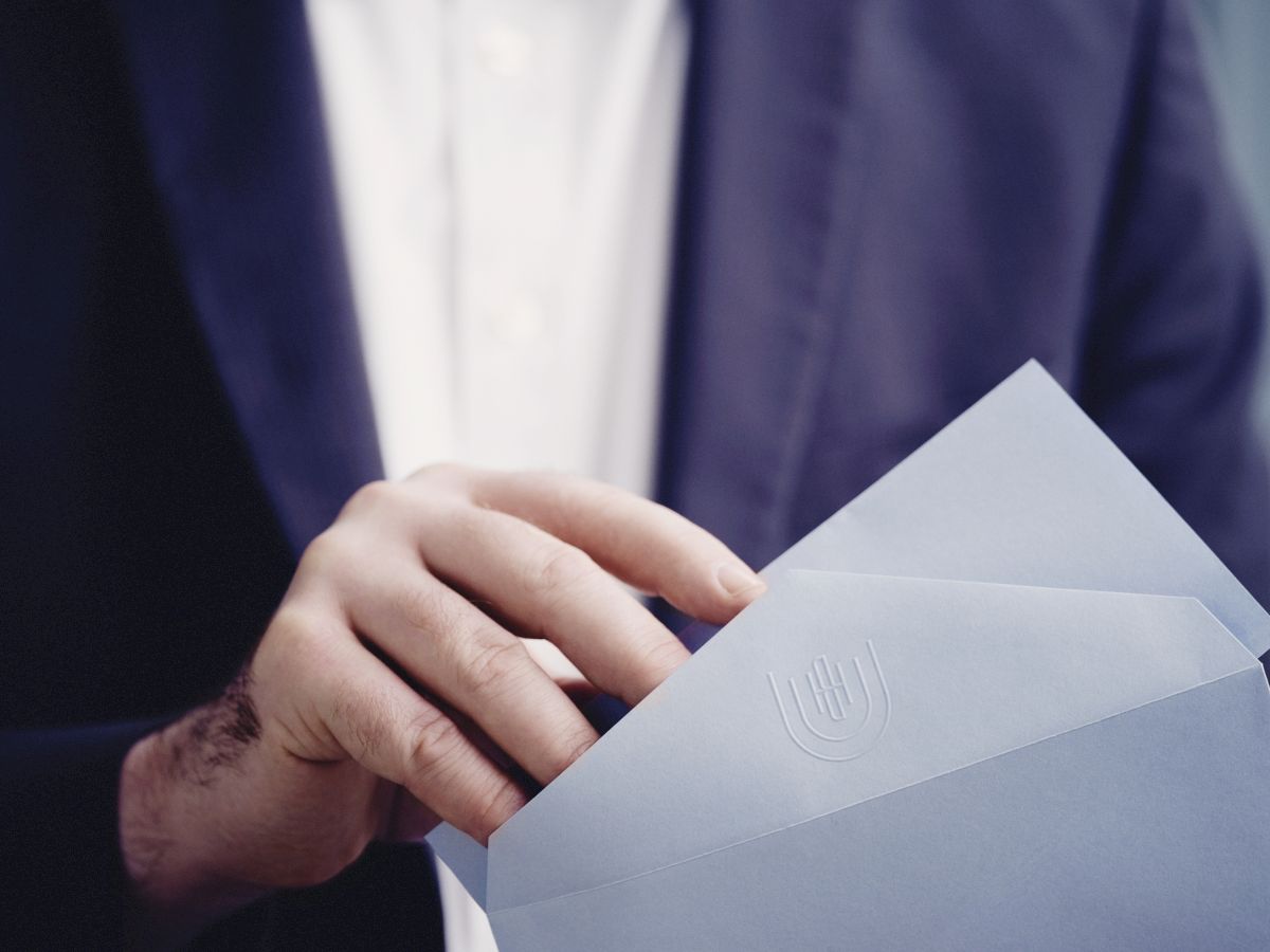 A person in a suit with a bow tie is holding an envelope.