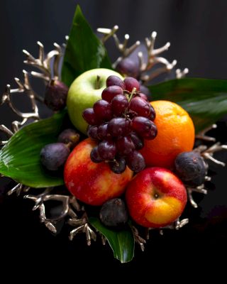 An assortment of fresh fruits with leaves, artistically arranged on a dark background.