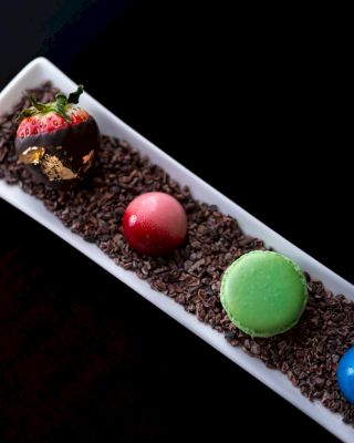A dessert with a chocolate-dipped strawberry and colorful macarons on chocolate sprink