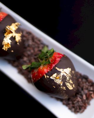 Gourmet chocolate desserts garnished with strawberries and gold leaf.
