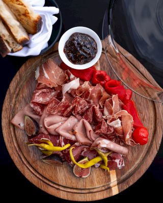 Charcuterie board with cured meats, peppers, tomatoes, dip, and bread
