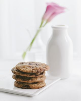 Stack of cookies on a plate, a milk bottle, and a pink flower in