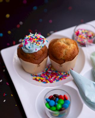 Two cupcakes with sprinkles, candy, and a piping bag on a white plate