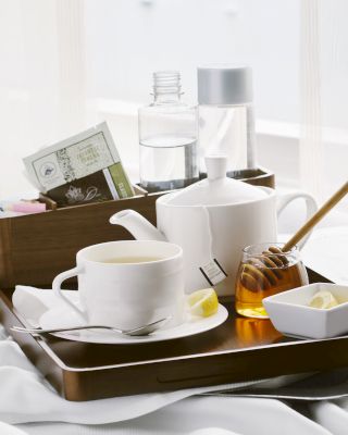 A breakfast tray with cups, a teapot, honey, and a newspaper on