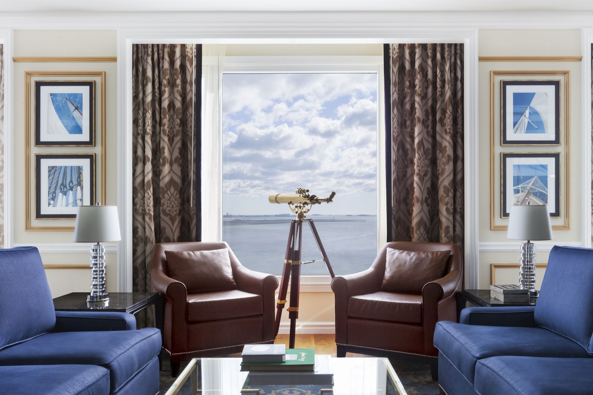 Elegant room with ocean view, two blue sofas, a telescope, and framed art.