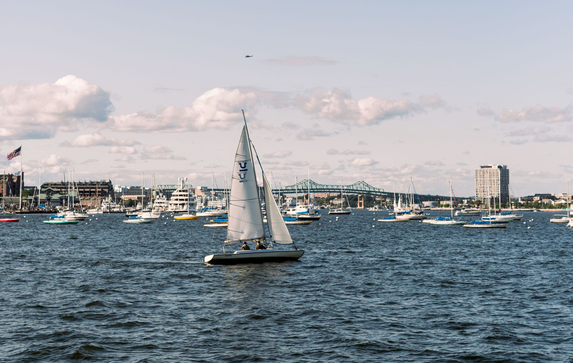 A sailboat on the water with a city skyline and blue sky in the background