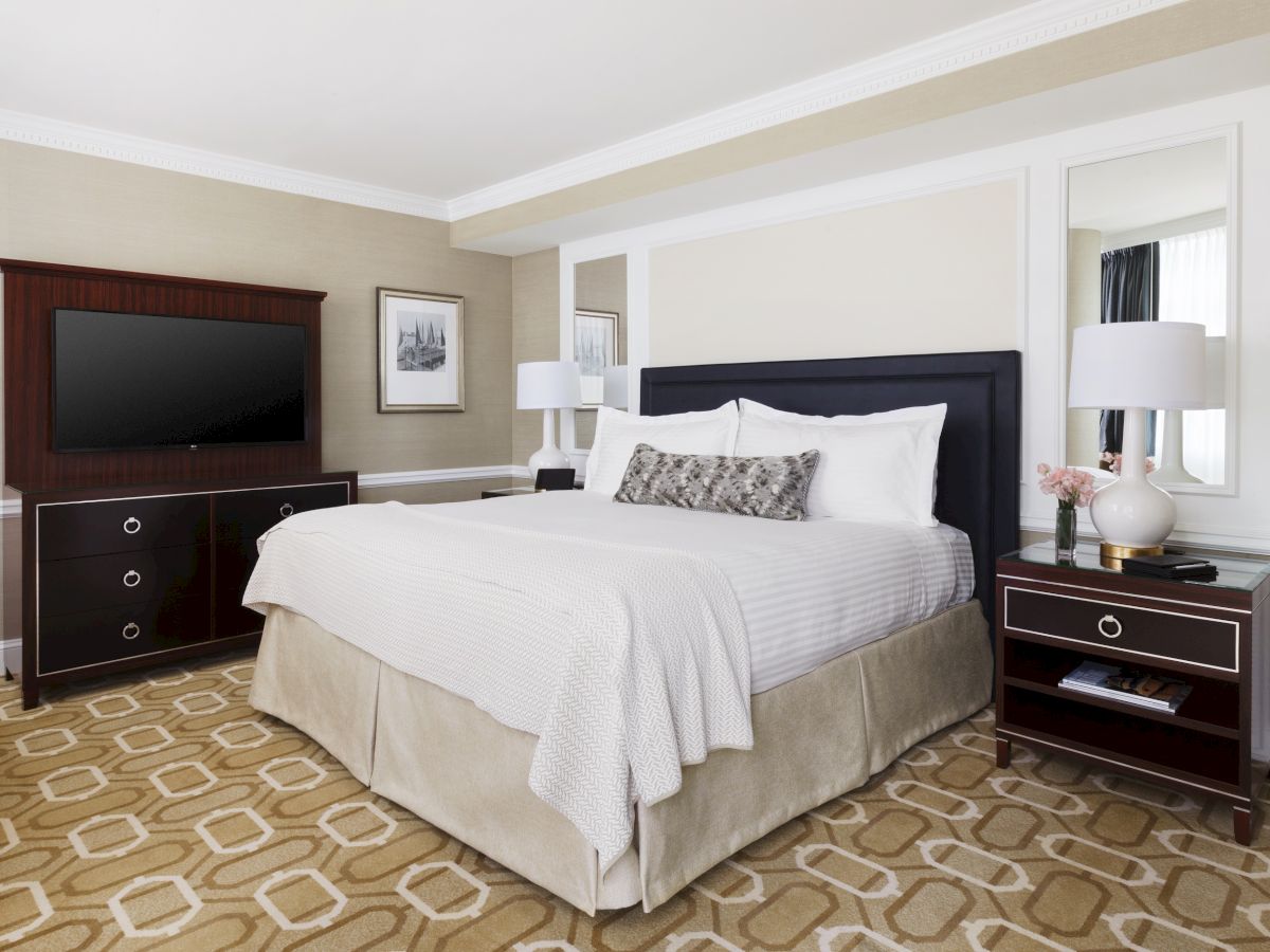 An elegant bedroom with a large bed, side tables, lamps, a chair,