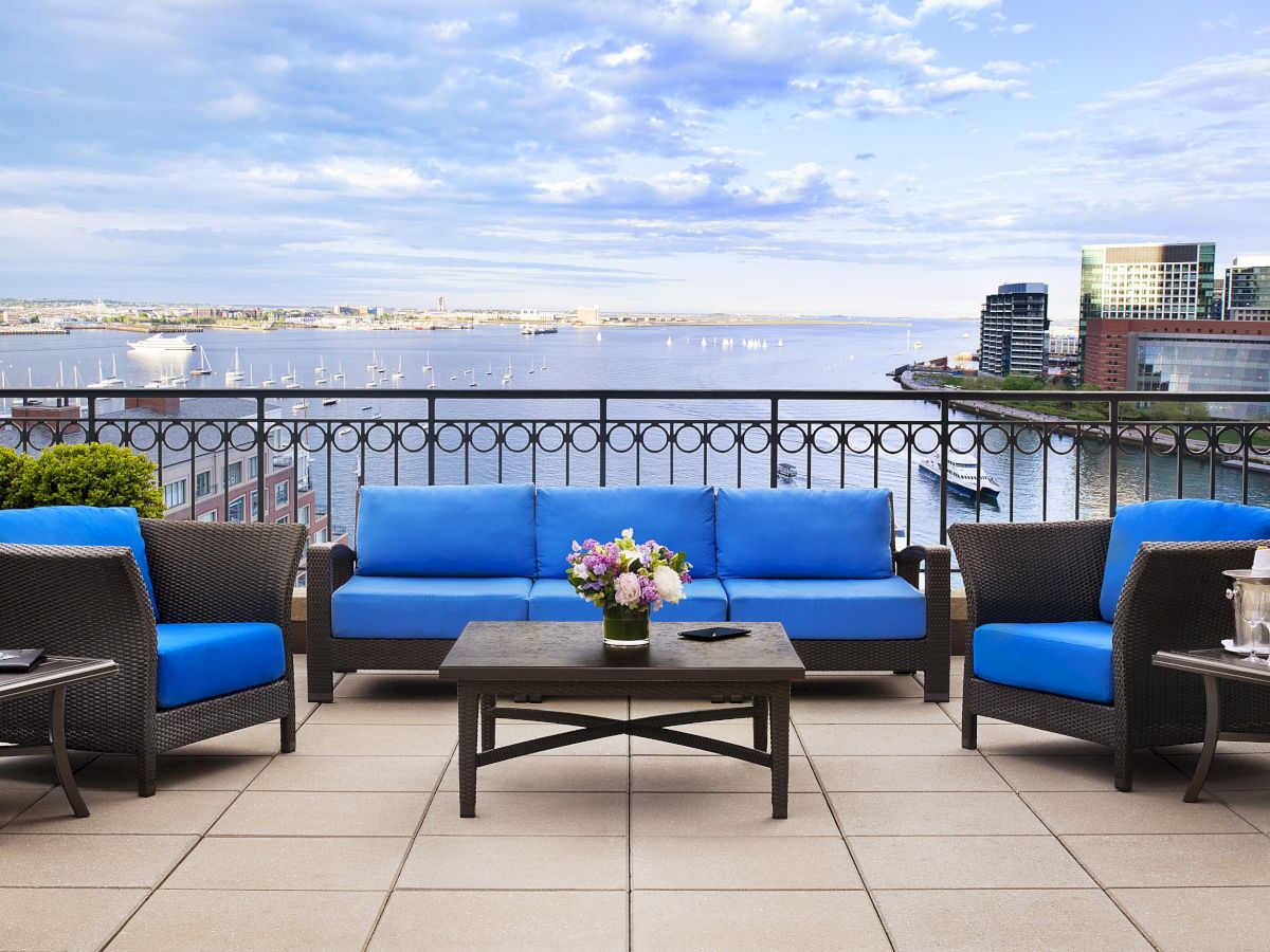 A waterfront balcony with blue sofas, a table, plants, and a city view.