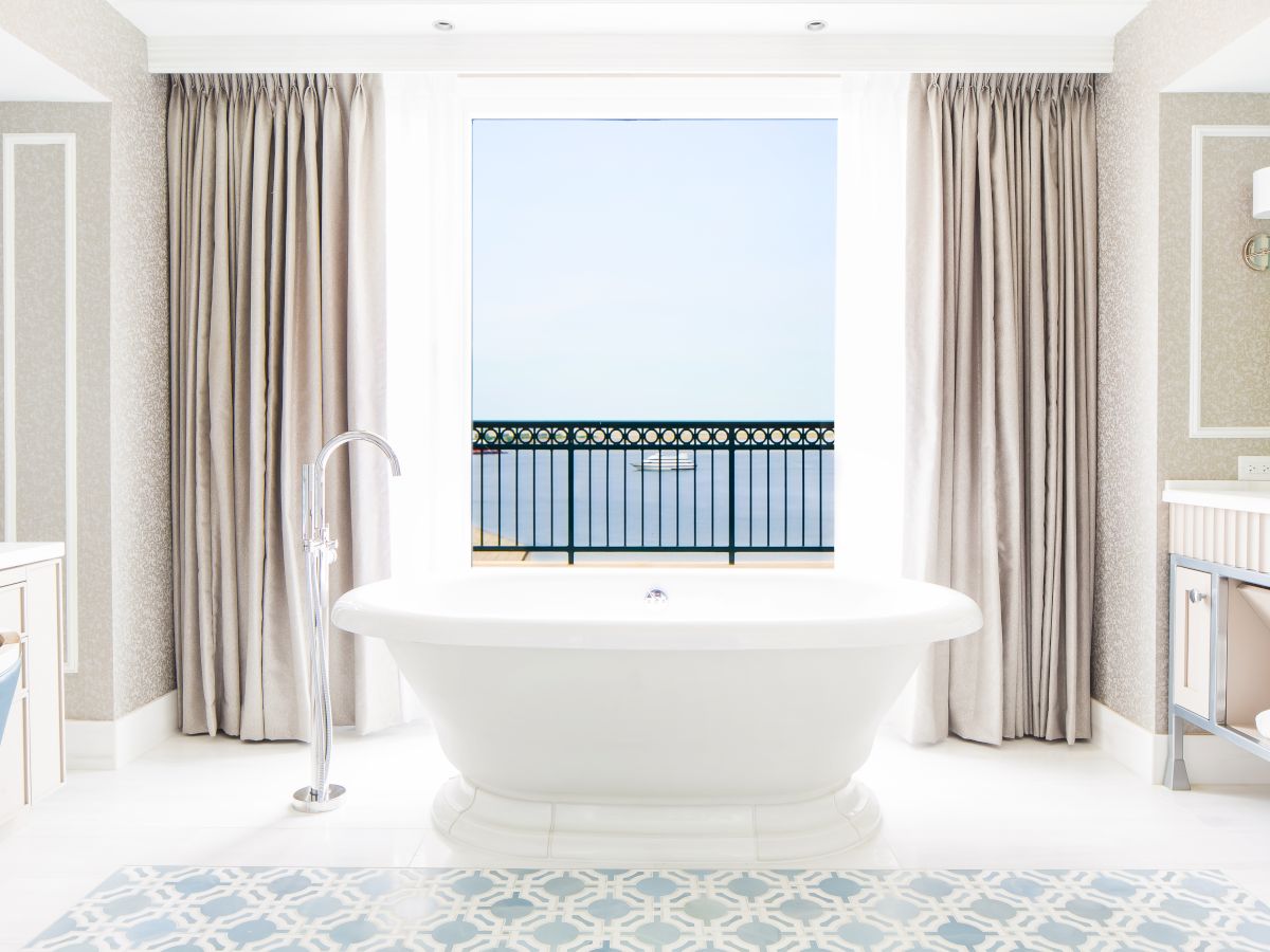 A bright bathroom with a freestanding tub, patterned floor, and curtains