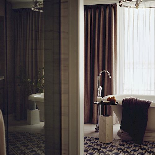 Elegant bathroom with a claw-foot tub, patterned floor, and sheer curtains
