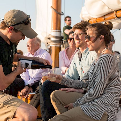 A person is pouring a drink for a woman on a boat with several people enjoying the setting.