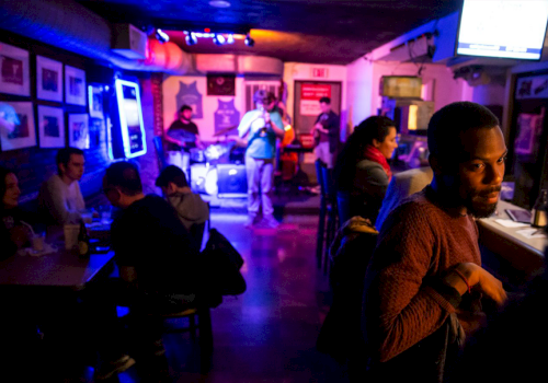 People are in a dimly lit bar with a band performing in the background, creating a lively and social atmosphere.