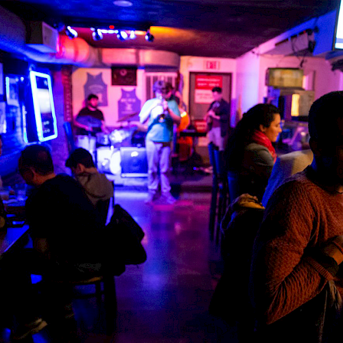 People are in a dimly lit bar with a band performing in the background, creating a lively and social atmosphere.