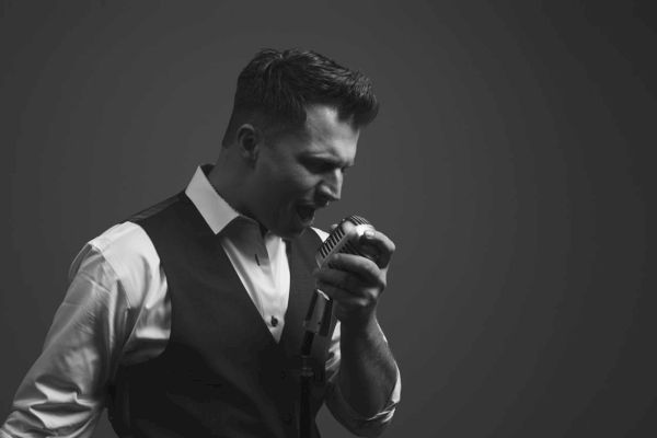 Black and white photo of Rich DiMare who is holding a microphone and singing