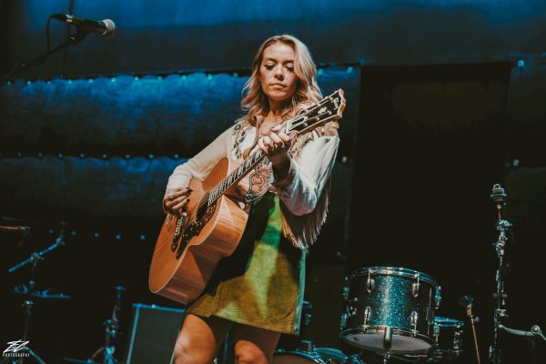 Musician Amanda Stewart playing the guitar on stage in front of a band.