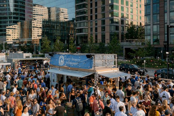 Outdoor event with a crowd, food truck, and modern buildings.