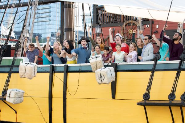 Guests on a yellow ship reenacting the throwing of the tea into Boston Harbor.