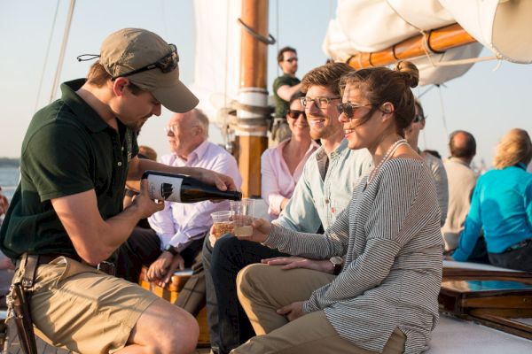 A group of people is enjoying a boat ride while a server pours a drink for a woman in a striped shirt.