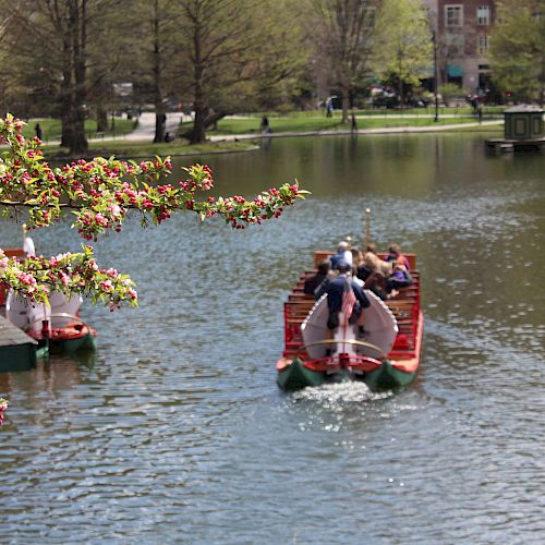 A group of people are enjoying a boat ride on a serene lake surrounded by greenery and blossoming tree branches in springtime.