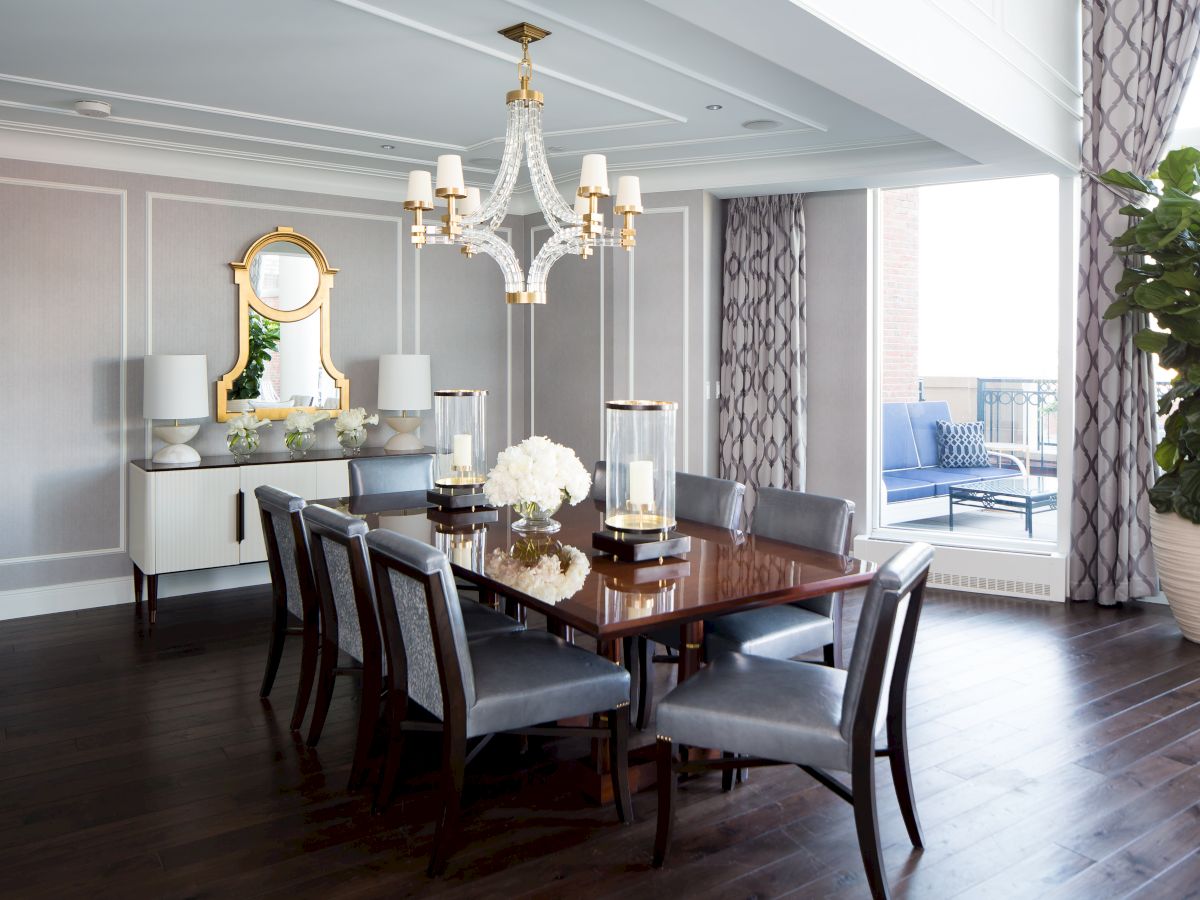 A stylish dining room with a chandelier over a table set for six. There's a large plant, a sideboard with a mirror, and a view to a balcony.